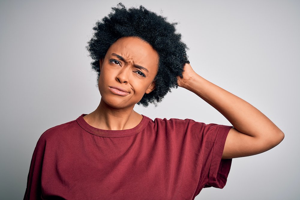 Young beautiful African American afro woman with curly hair wearing casual t-shirt standing confuse